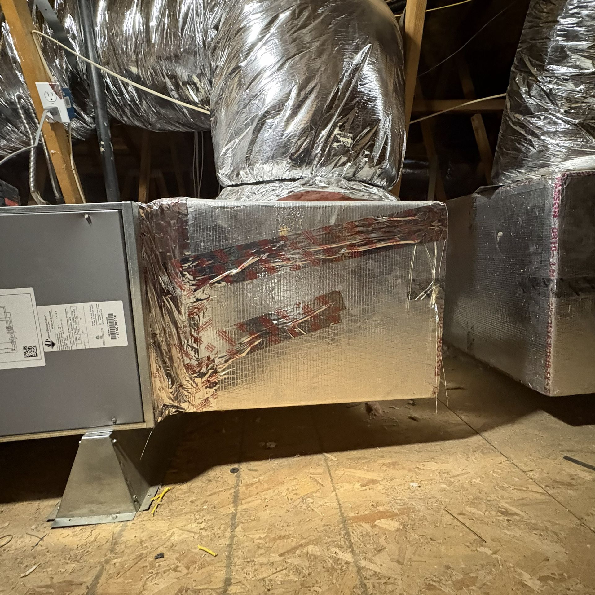 Insulated HVAC ductwork in an unfinished attic with reflective silver wrapping and metal supports