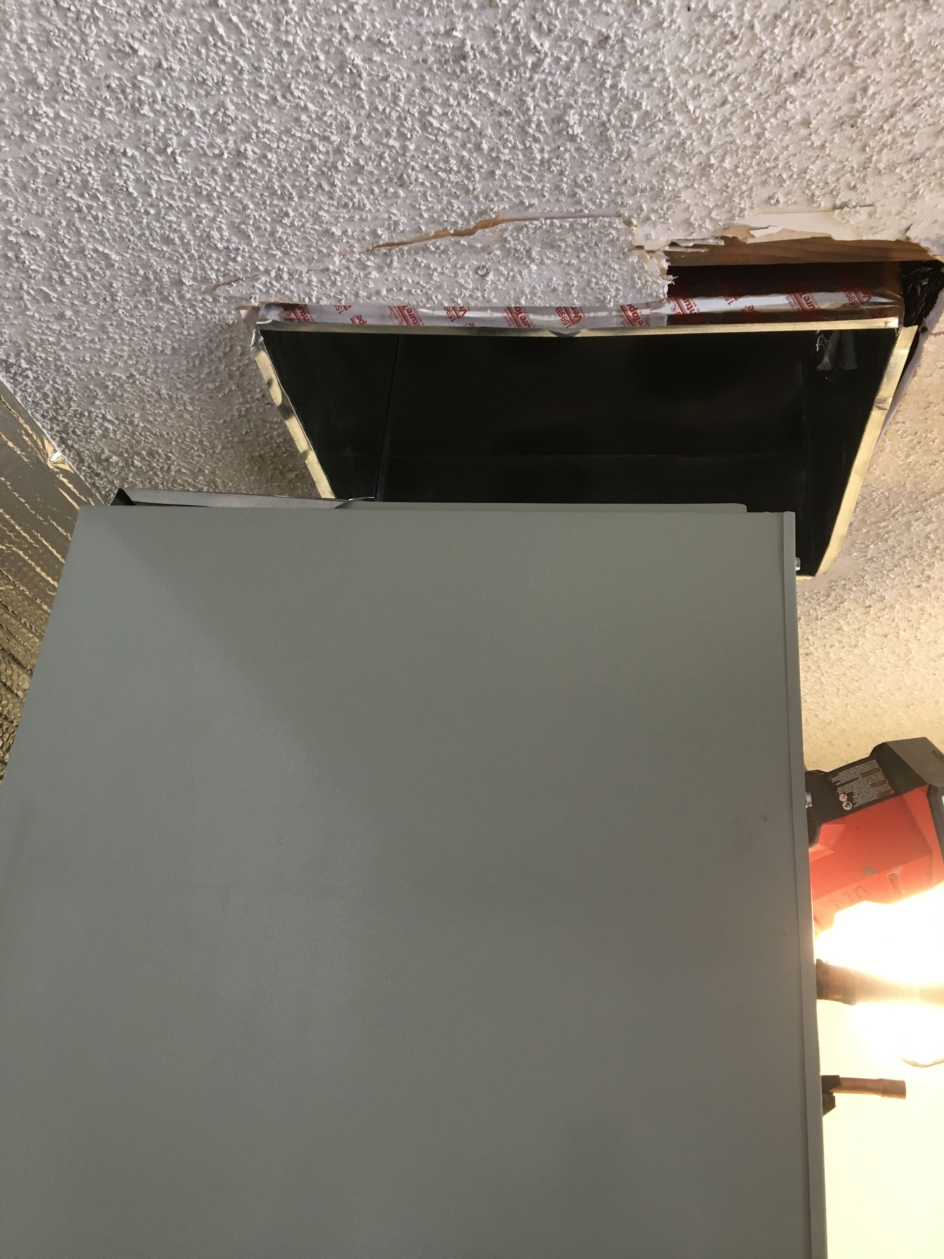 Broken ceiling with a dark opening above a gray cabinet, lit by a bright lamp on the right.