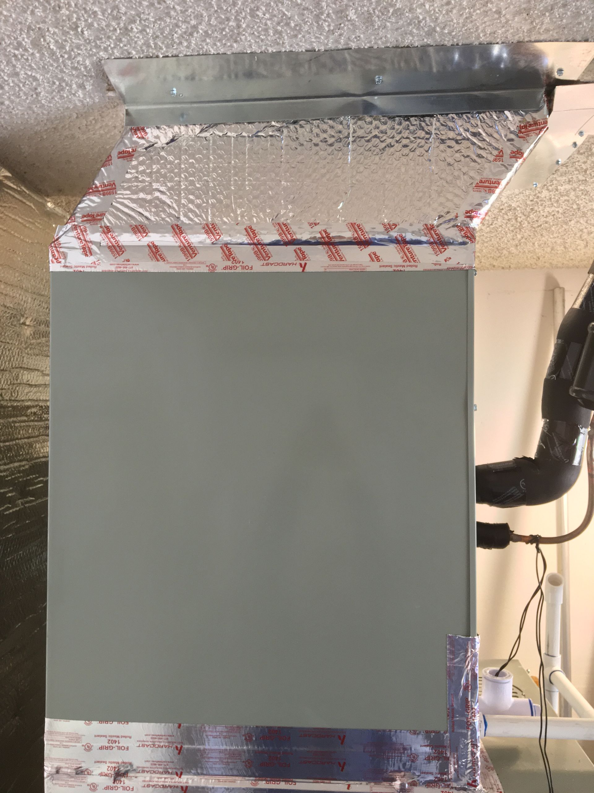 Large gray HVAC duct or cabinet under a metal ceiling vent with exposed piping and insulation.