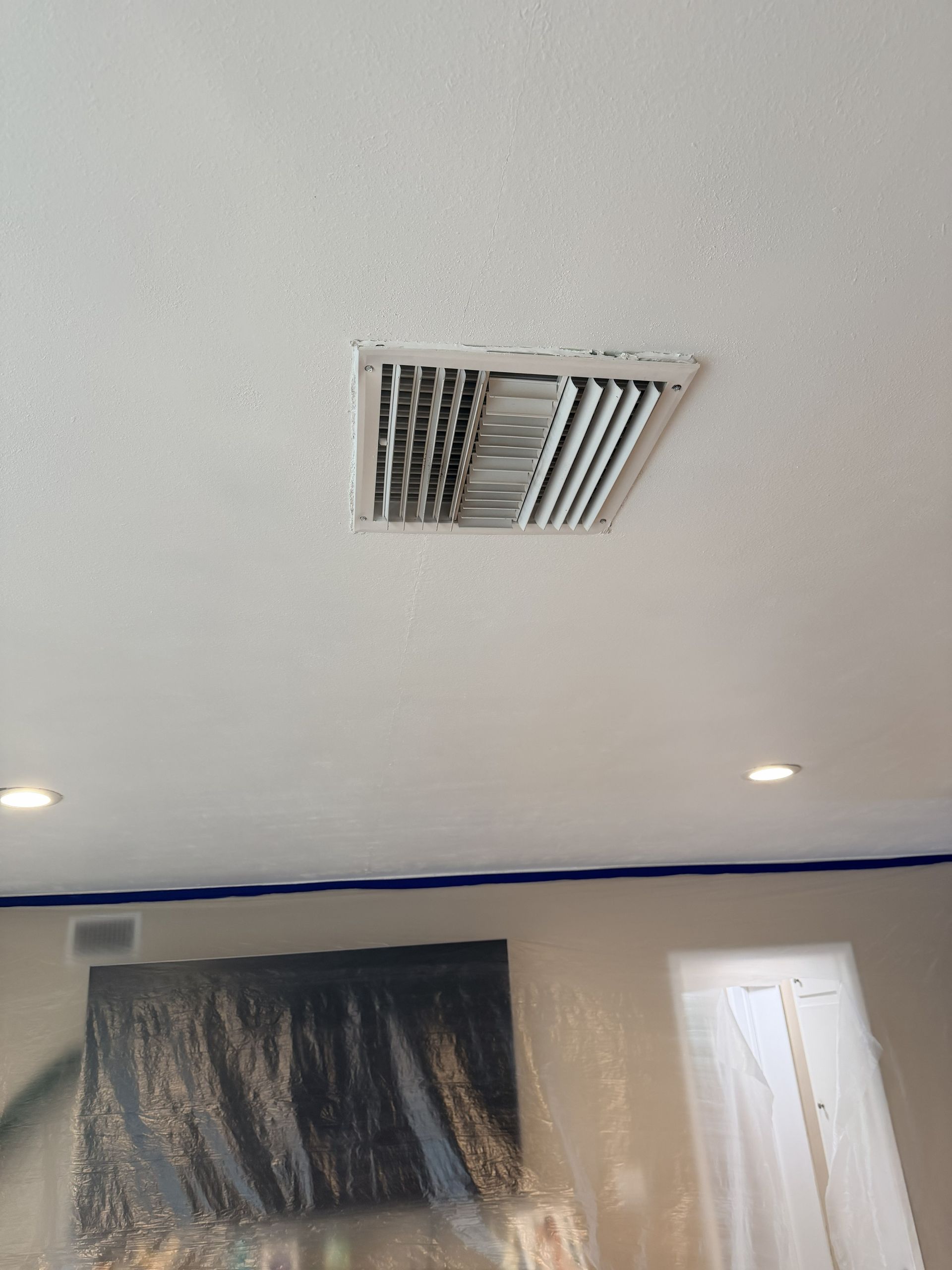 Ceiling air vent above a room with blue tape along the wall and a covered window.