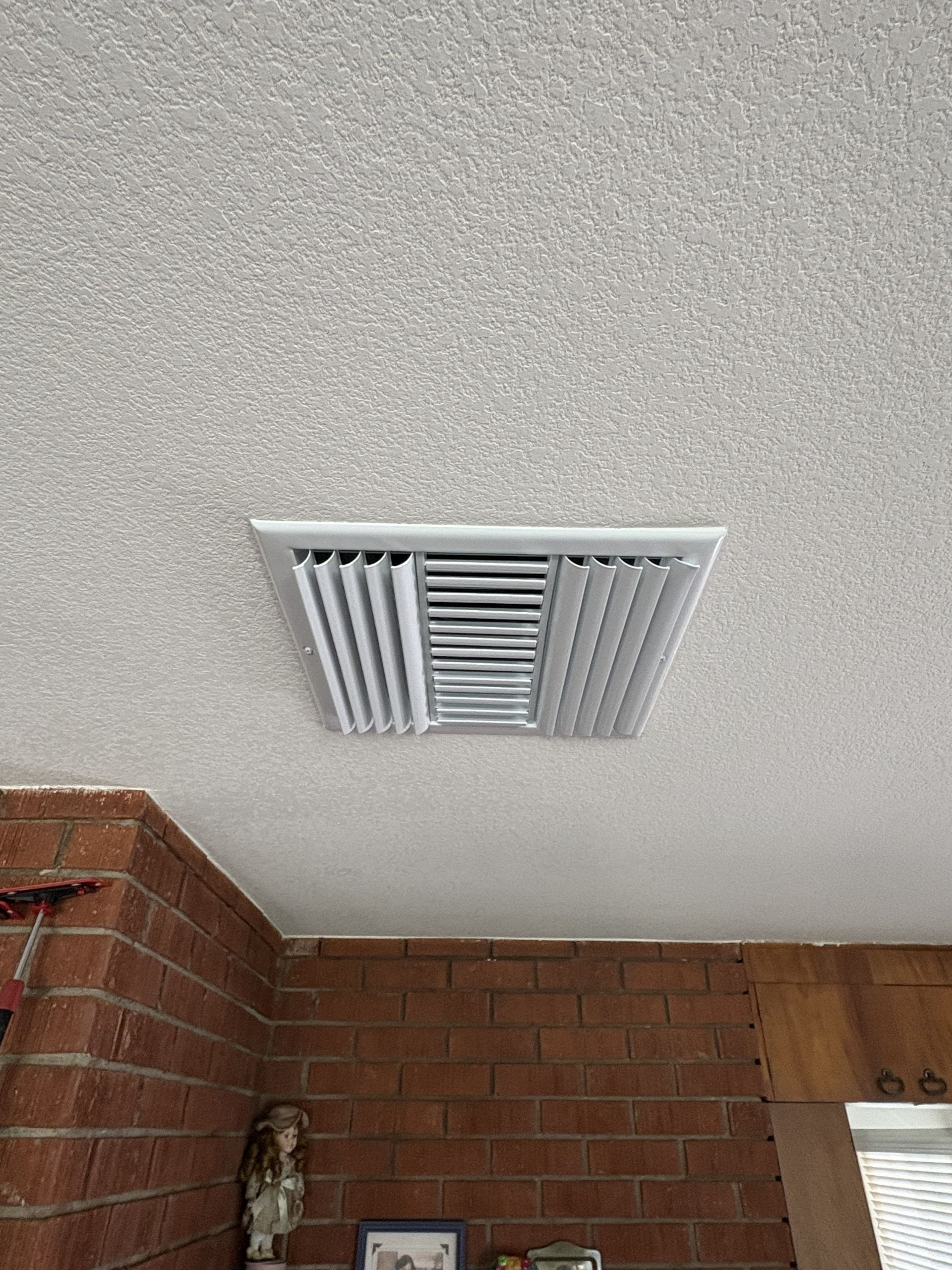 Ceiling air vent on a textured white ceiling above a brick wall corner and doorway