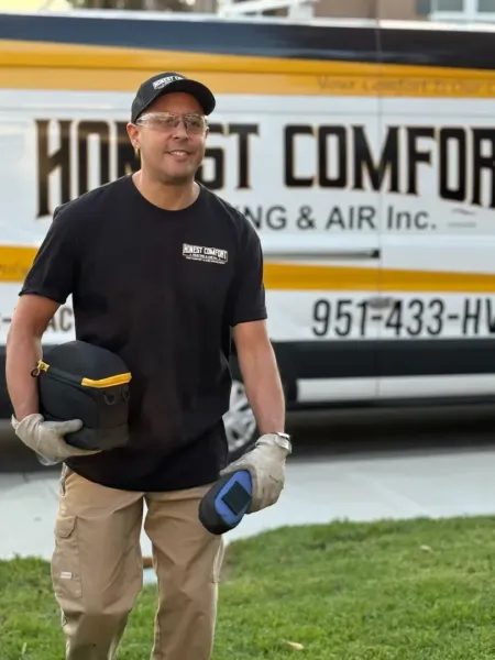 Man in black shirt and tan pants holding a tool bag, standing in front of a heating and air service van.
