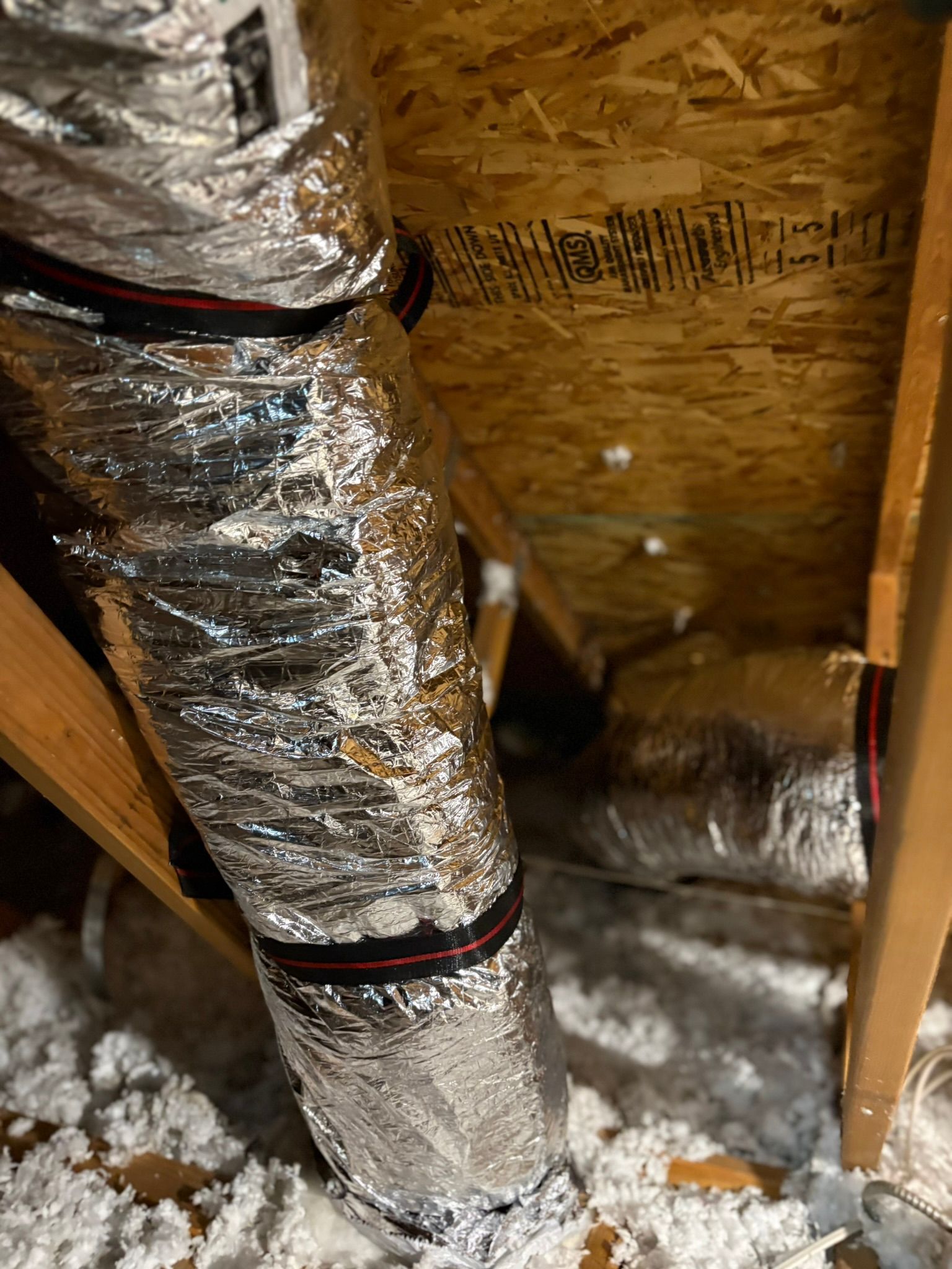 Insulated HVAC ductwork in an attic with foil wrap and wooden framing