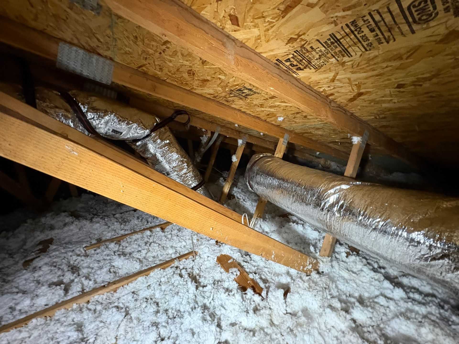 Insulated attic with exposed wooden rafters and a thick layer of loose white insulation on the floor