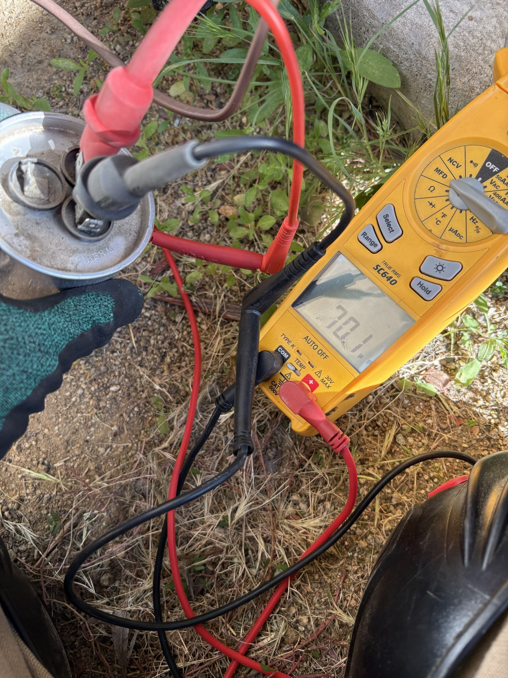 Yellow multimeter testing a plugged-in metal canister with red and black probes outdoors