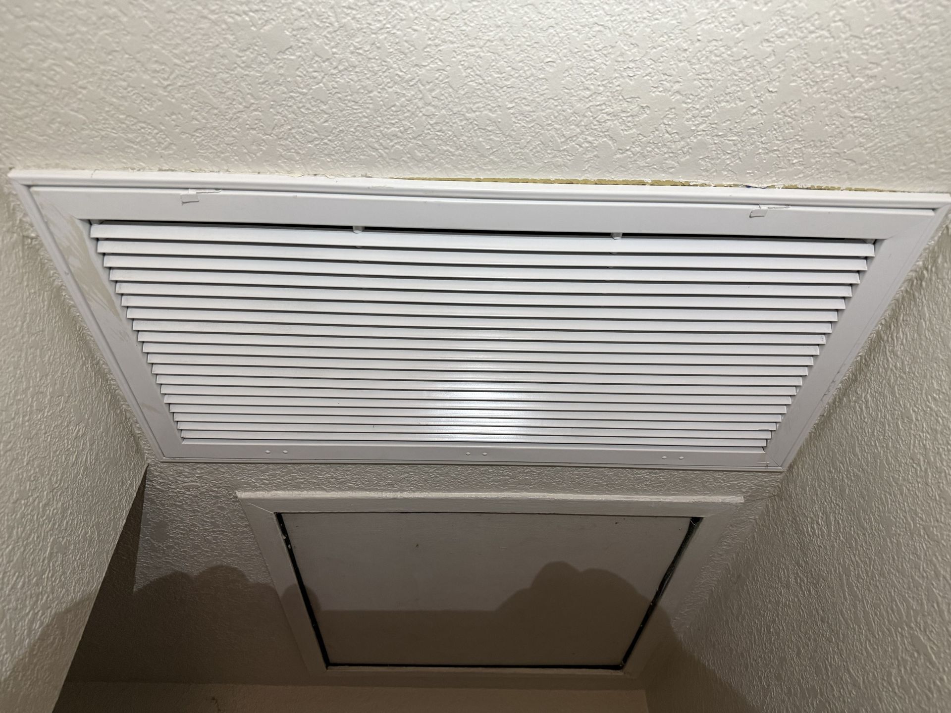 Ceiling vent and attic access panel in a beige hallway ceiling