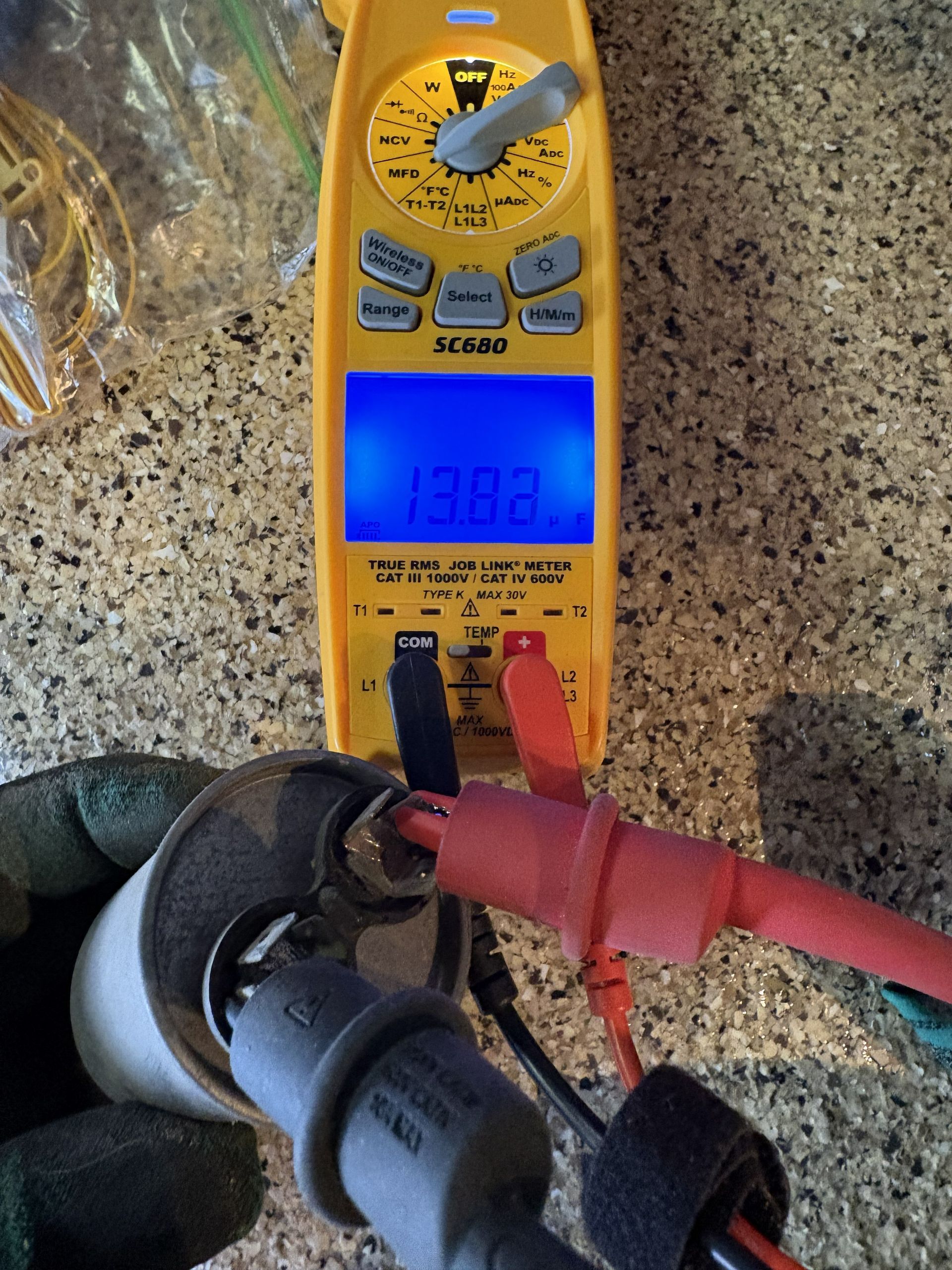 Yellow digital multimeter measuring voltage on a red-handled cable near a floor outlet。