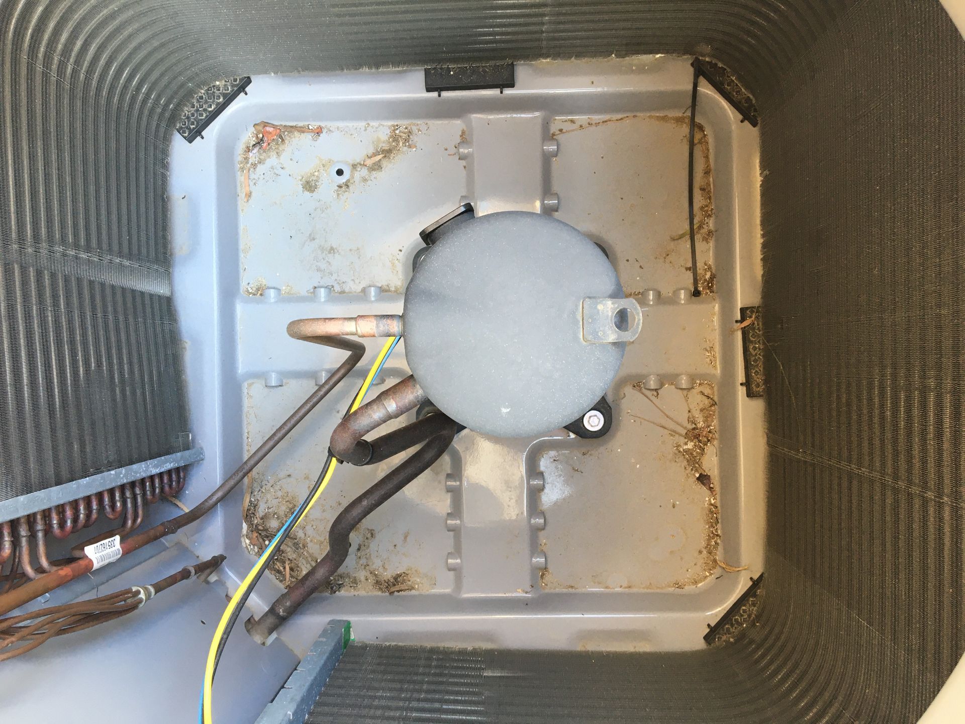 Inside an HVAC unit, a round gray blower motor with wires and metal housing.