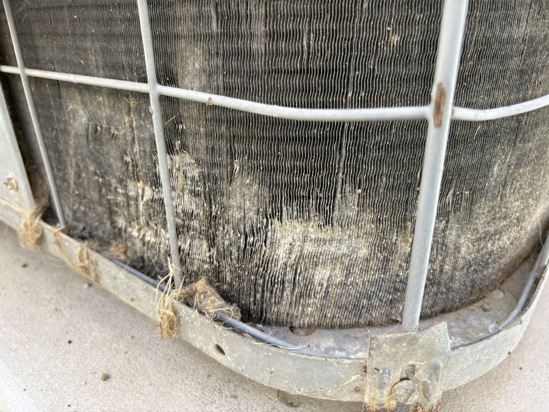 Close-up of a rusted metal cage around a dirty HVAC unit outdoors.