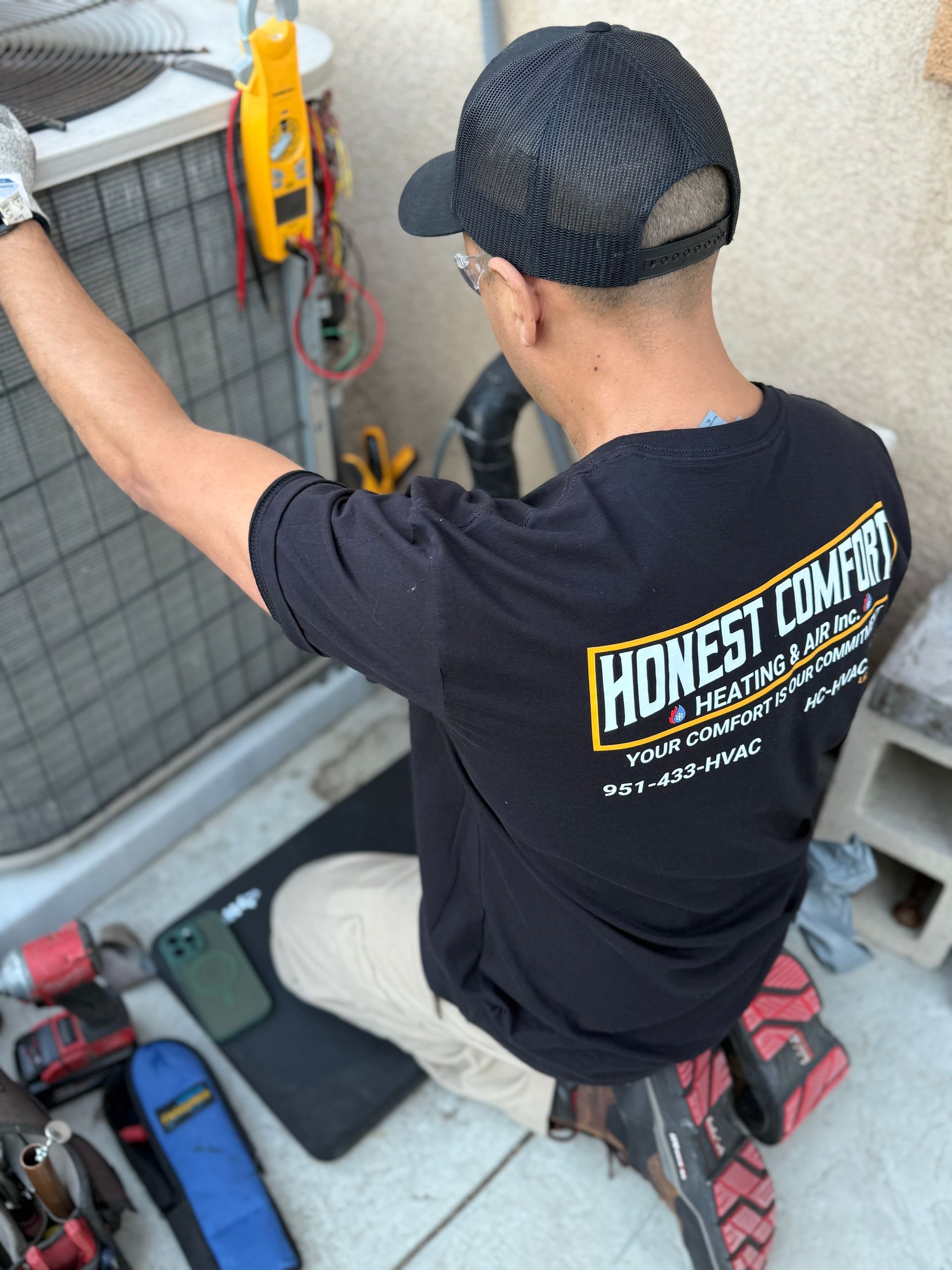 Worker in black shirt and cap repairing HVAC unit on a rooftop with tools nearby