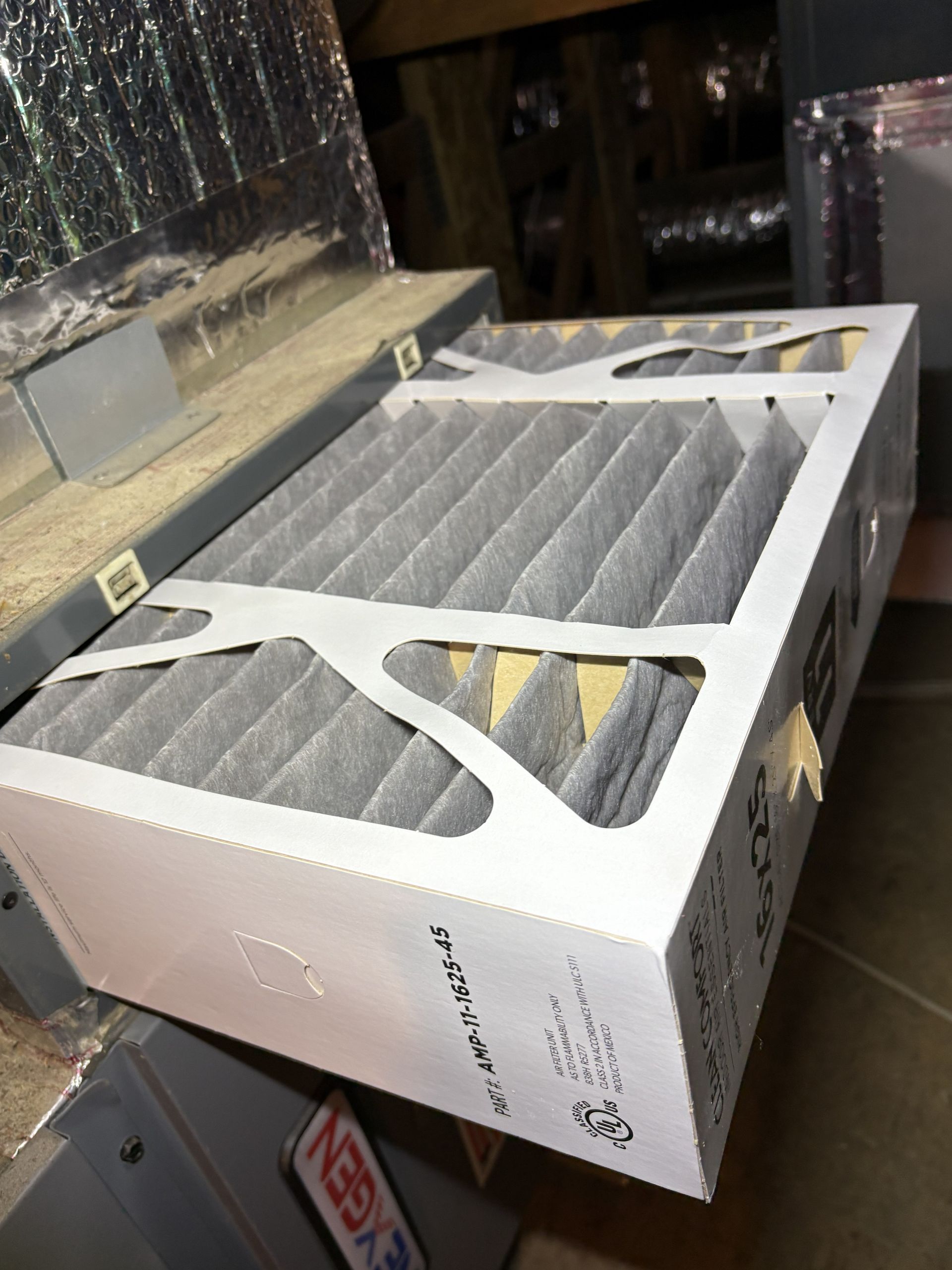 Dusty HVAC filter in a cardboard frame lying on a floor near equipment cabinets