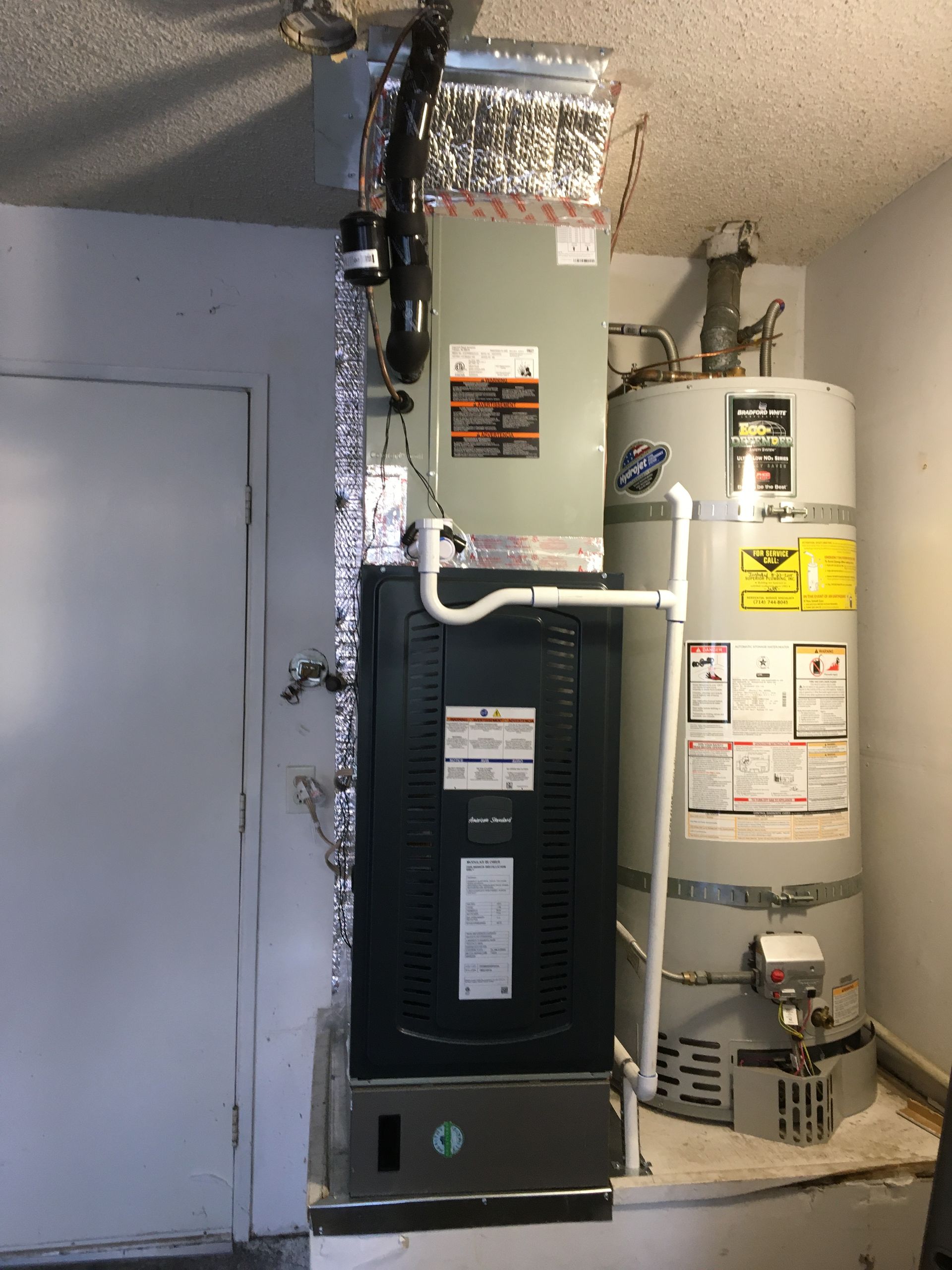 Residential furnace and water heater in a utility closet with exposed ductwork and pipes