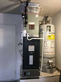 HVAC furnace and water heater in a utility closet with exposed ductwork and pipes