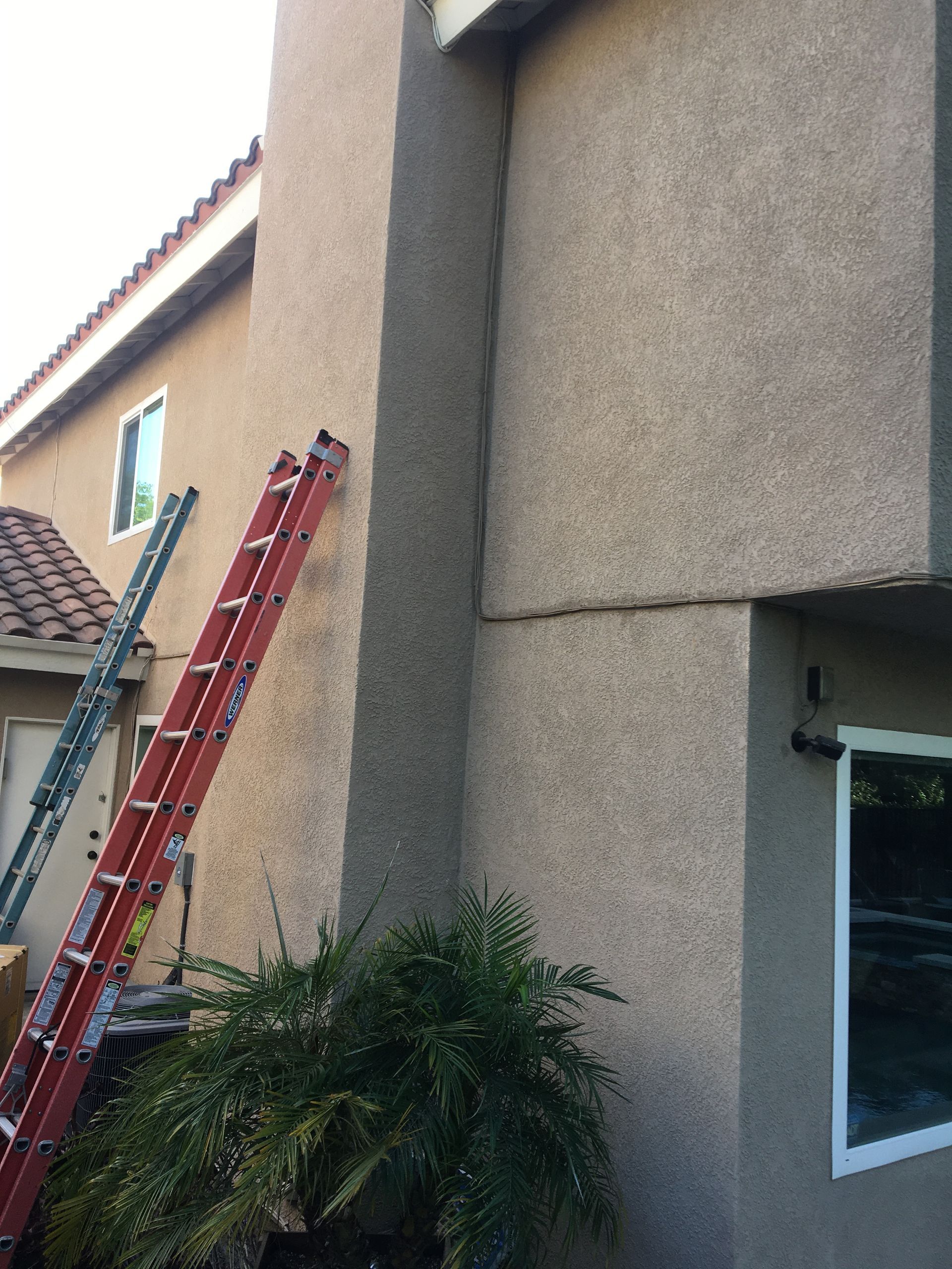 Two ladders leaning against a stucco house beside a window and roofline under repair