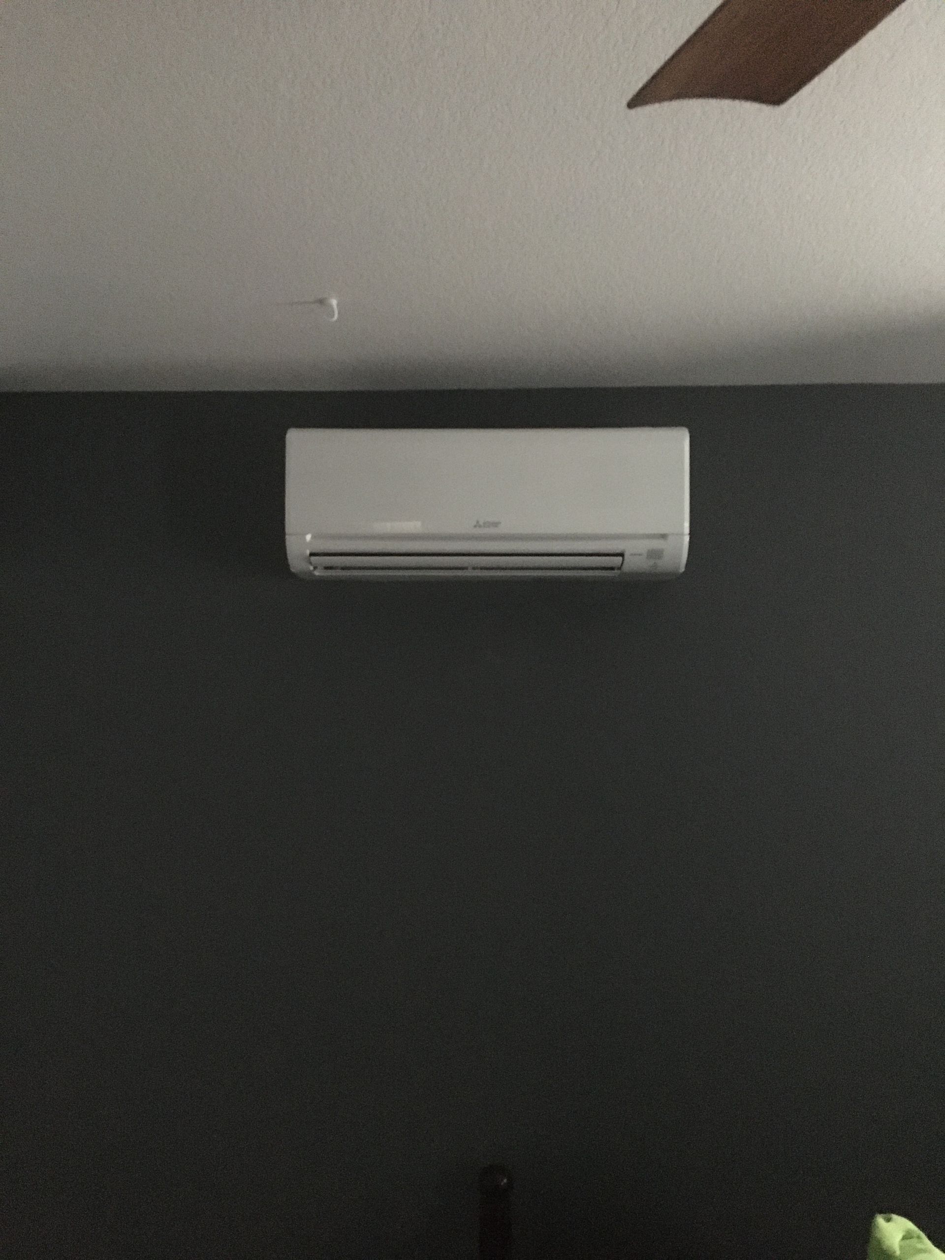 White wall-mounted air conditioner on a dark gray wall, with part of a ceiling fan visible above.