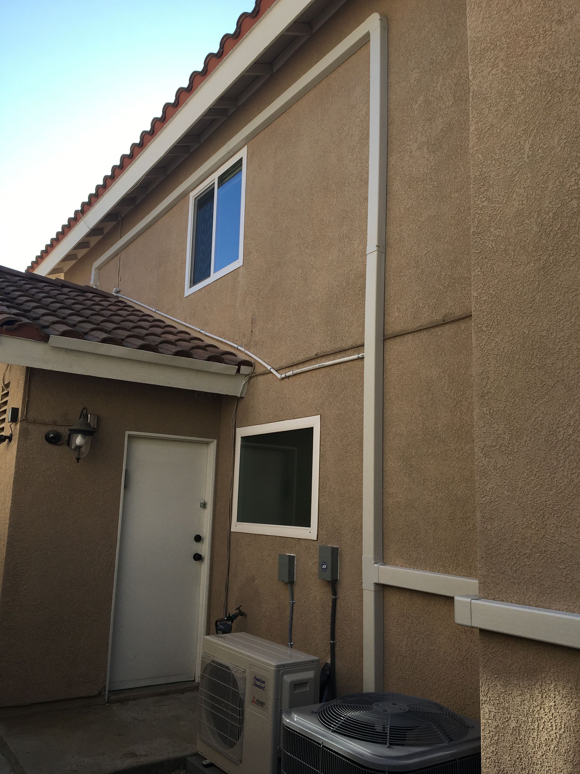 Narrow stucco house exterior with white trim, blue window, door, and two air conditioner units