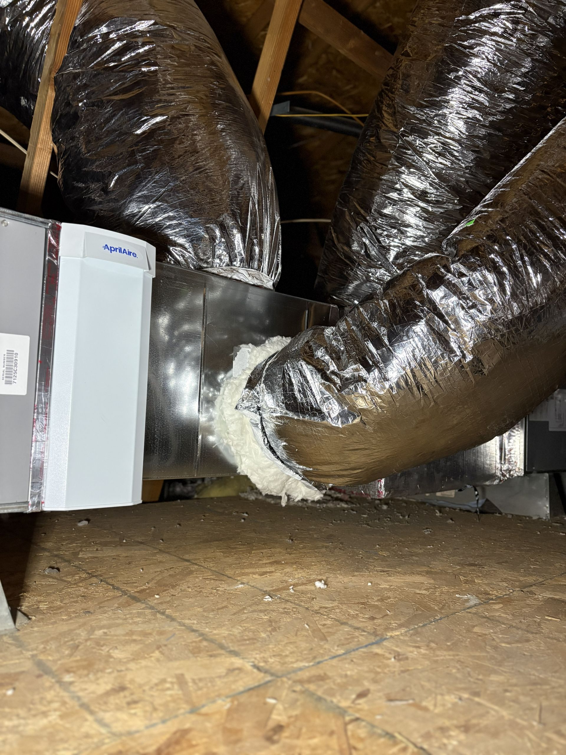 Attic HVAC unit with insulated ducts and a white sealant patch on the floor