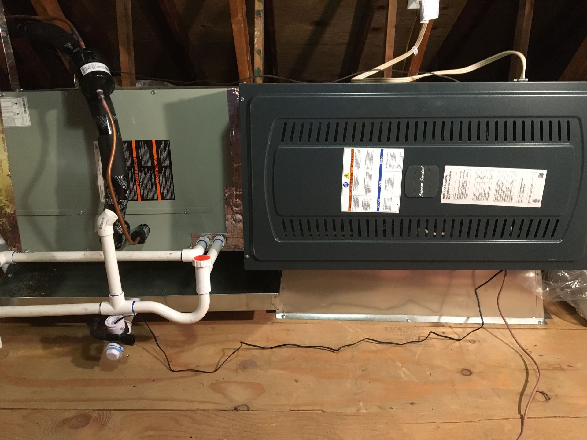 HVAC furnace and white PVC drain piping in a utility closet with exposed wiring and wood floor