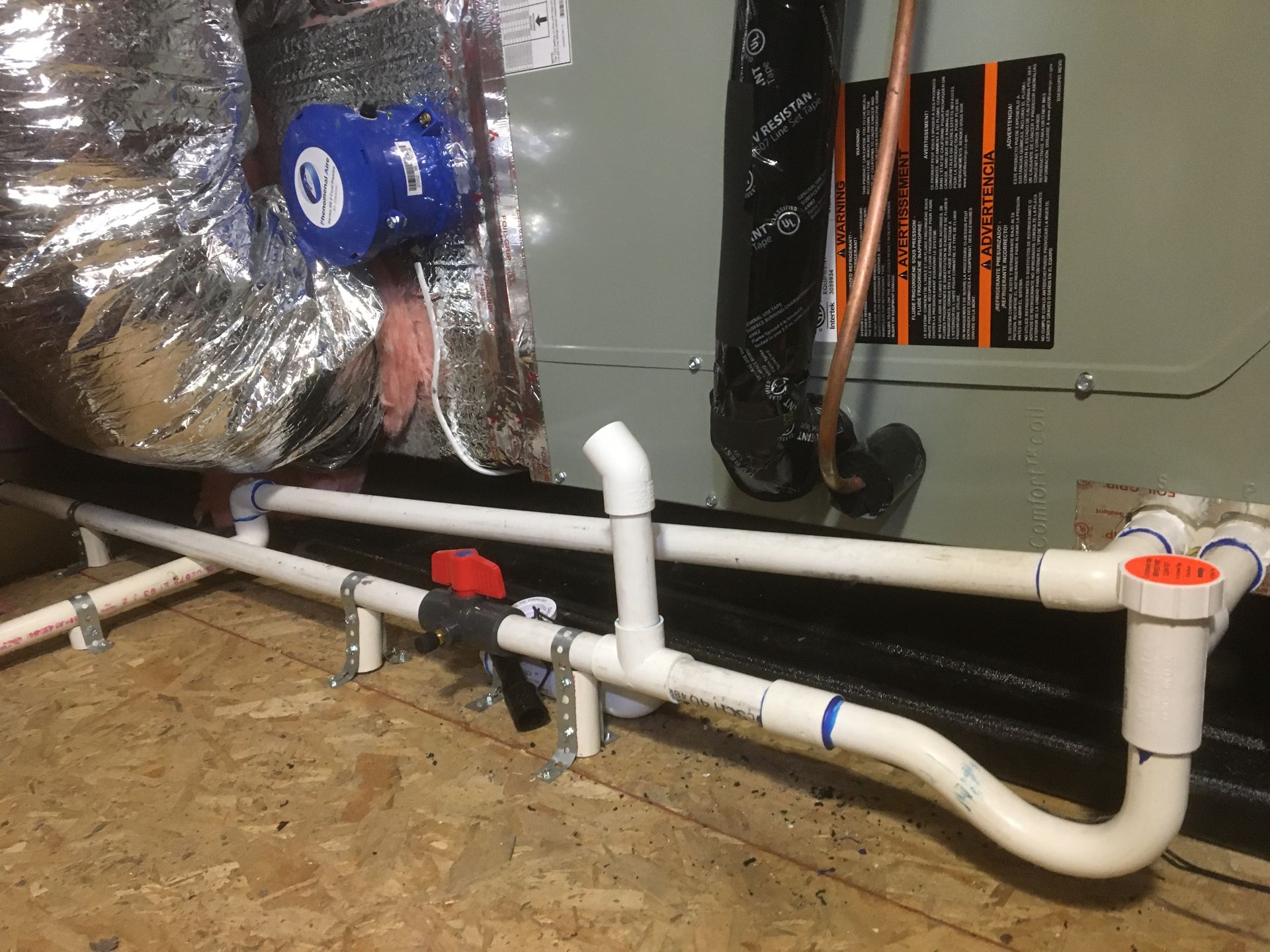 PVC drain pipes and fittings installed beside HVAC ducting in a utility space.