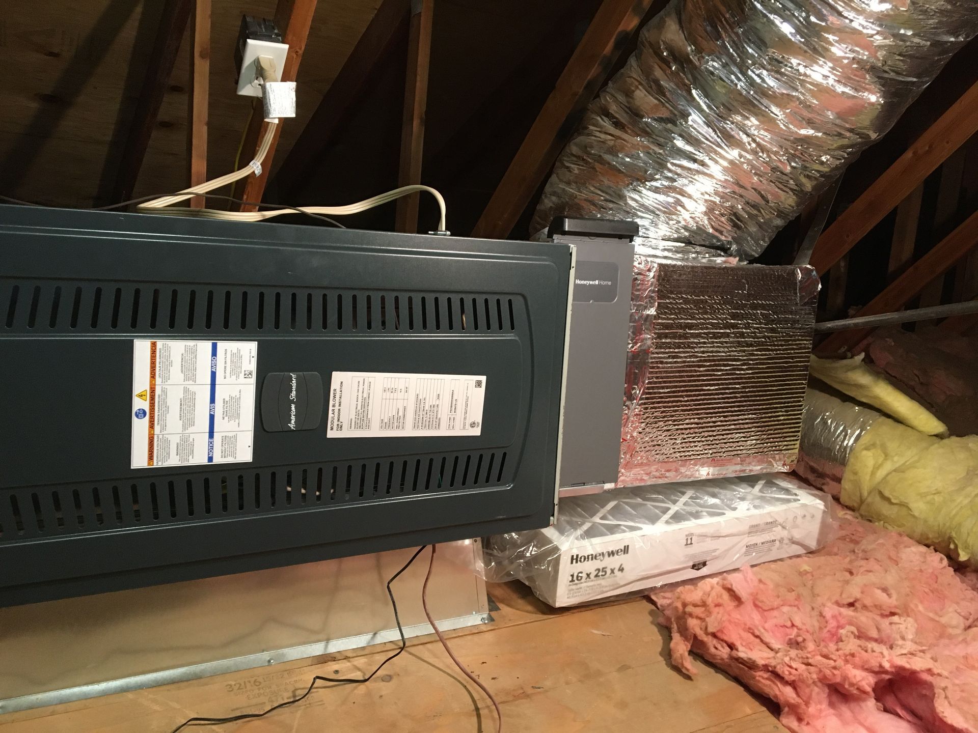 Attic HVAC unit with exposed ductwork and insulation under a sloped roof