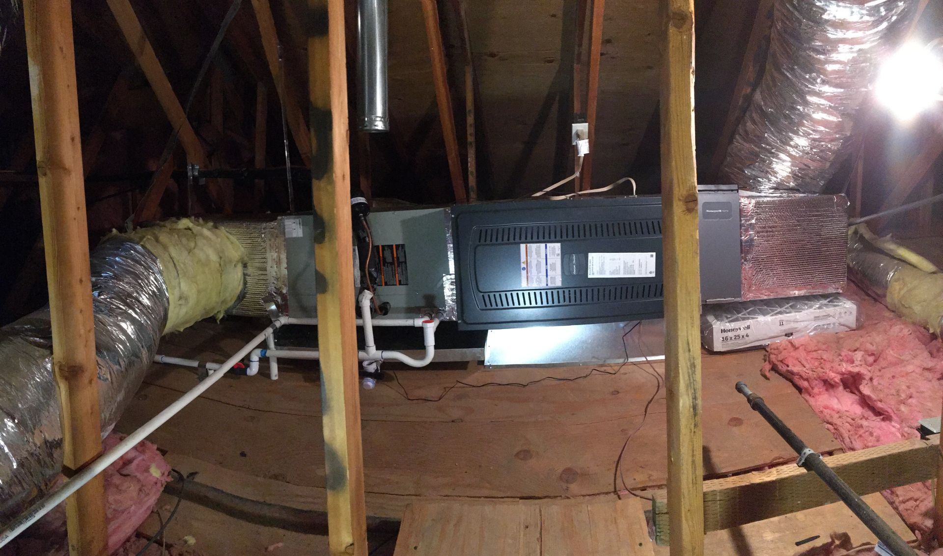 Attic HVAC unit with ductwork, insulation, and wooden rafters exposed in a crawlspace.