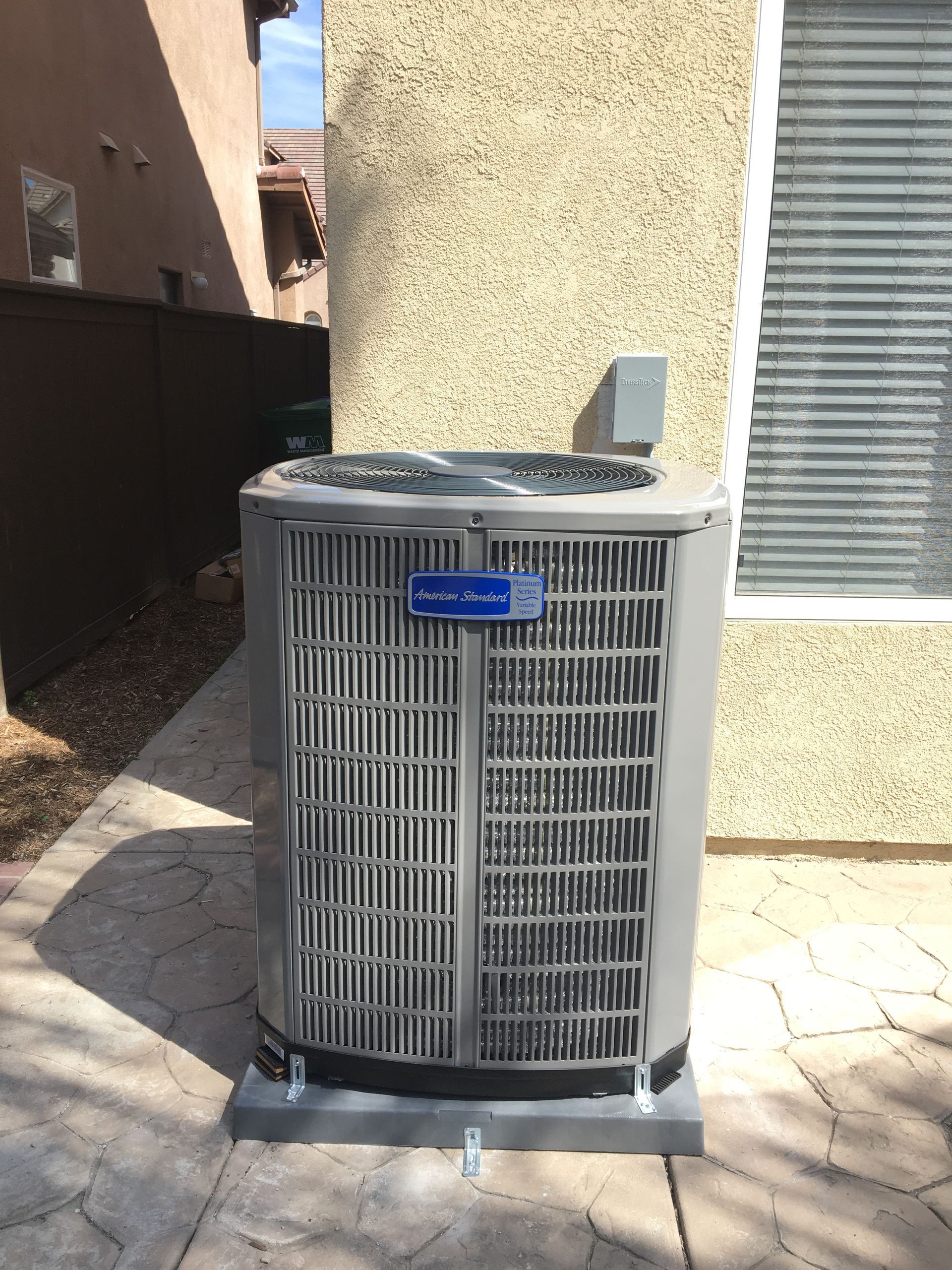 Outdoor air conditioner unit beside a beige stucco wall and window in a narrow side yard