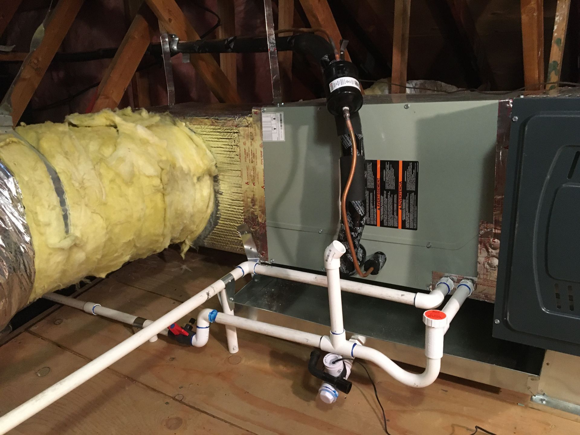 Attic HVAC unit with insulated ducts and white PVC pipes connected to a furnace system