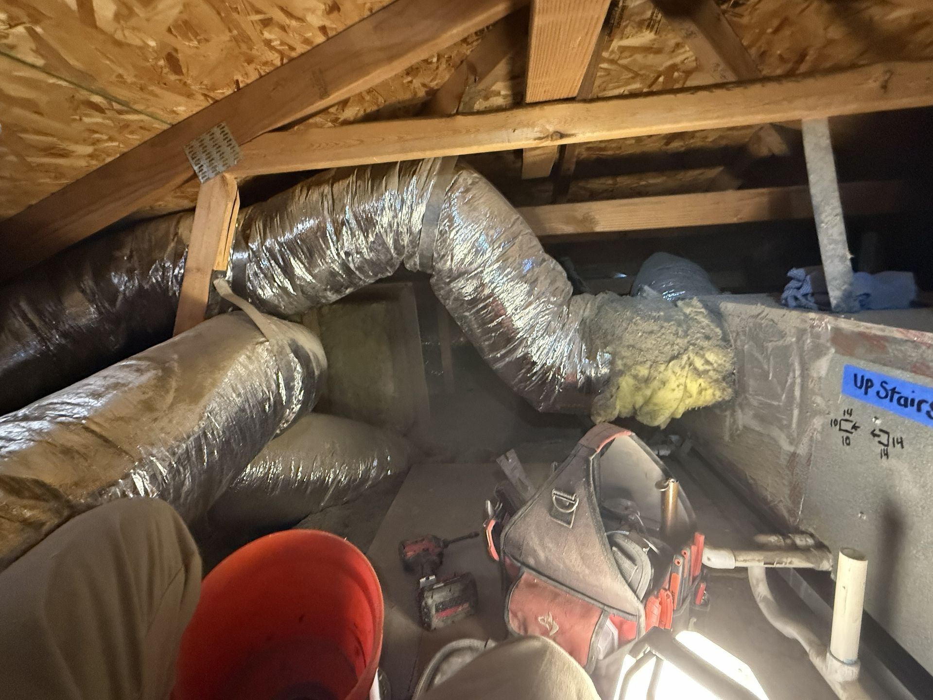 Attic with insulated ductwork, exposed rafters, and clutter including a red bucket and tools