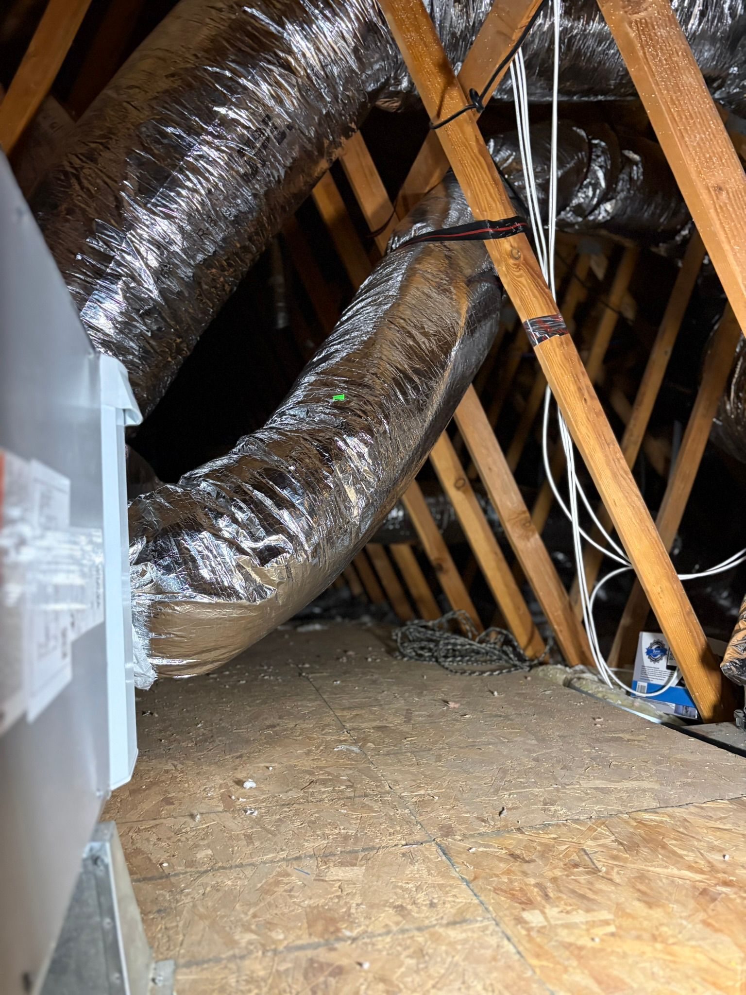 Attic with exposed wooden rafters and insulated ductwork running across the floor and ceiling.