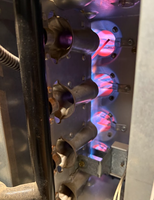 Close-up of a metal machine interior with glowing red-blue burners or heating elements