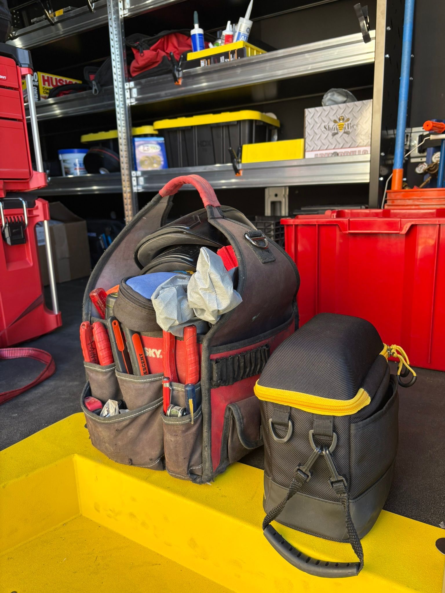 Red and black tool bags on a yellow shelf in a garage or workshop