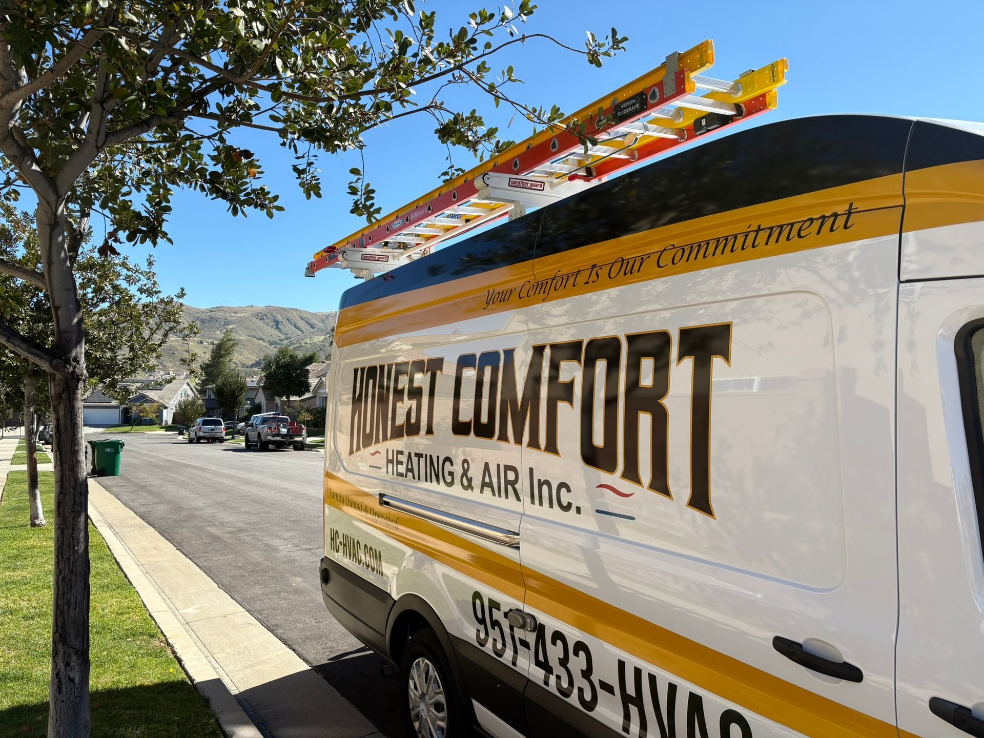 White HVAC service van parked on a sunny street, with “West Comfort” signage and a ladder on top.