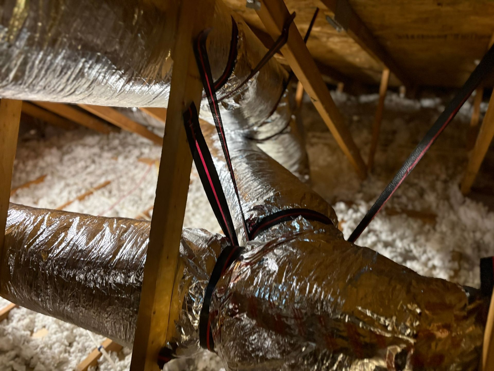 Wrapped HVAC ducts in an attic with insulation and support straps