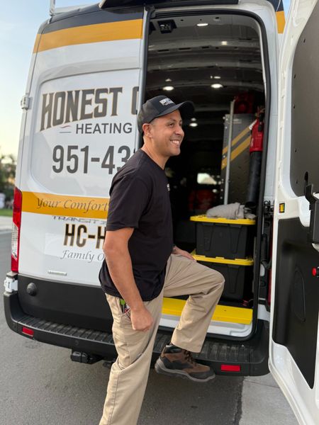 Man standing at the open rear of a white Honest Heating van, smiling and stepping in with tools inside.