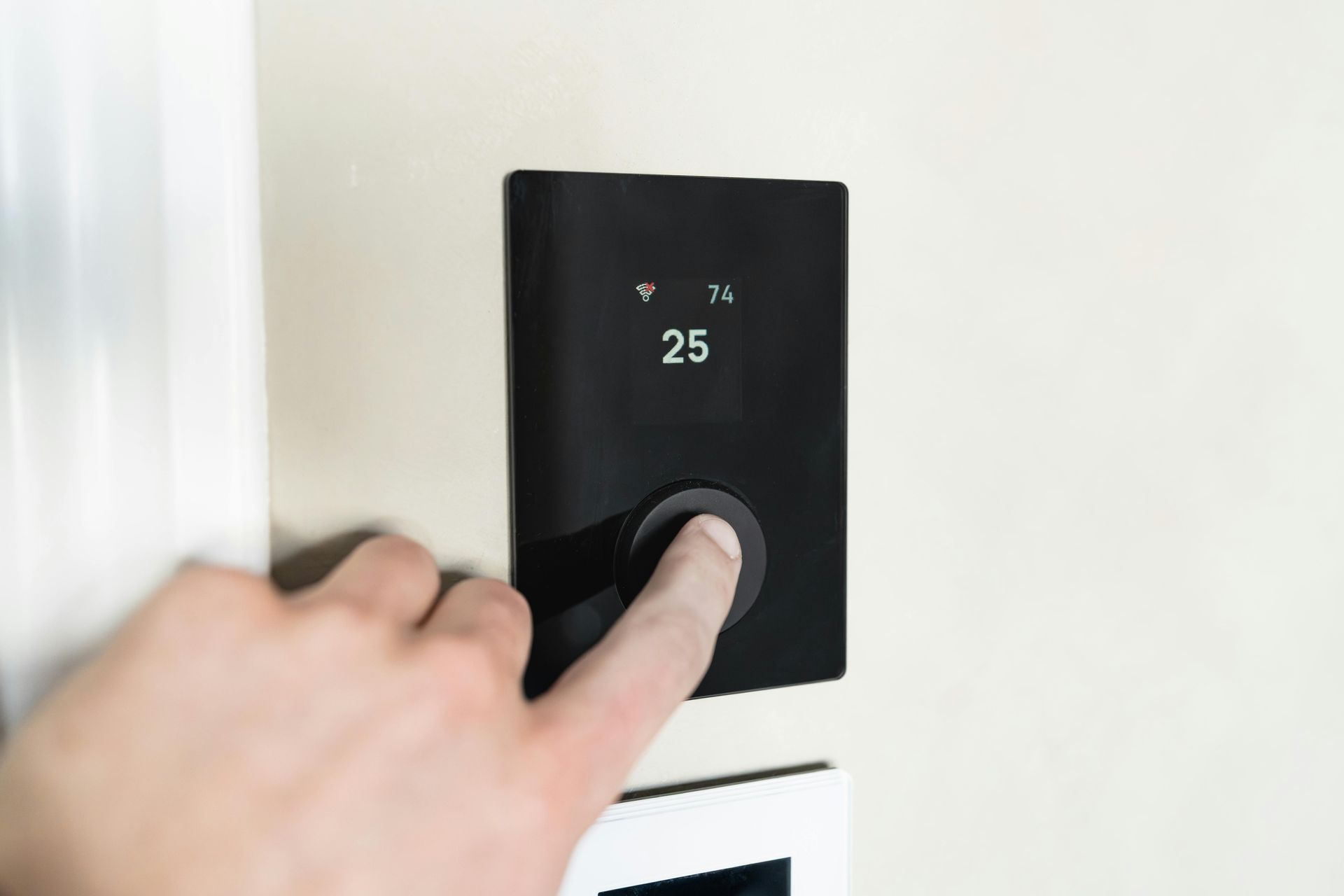 Hand pressing a black wall thermostat set to 25°C