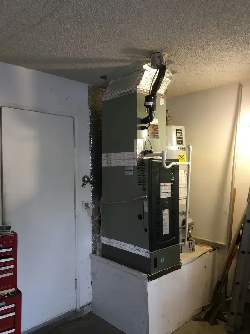 Water heater and furnace in a small utility room with a white door and red fire extinguisher.