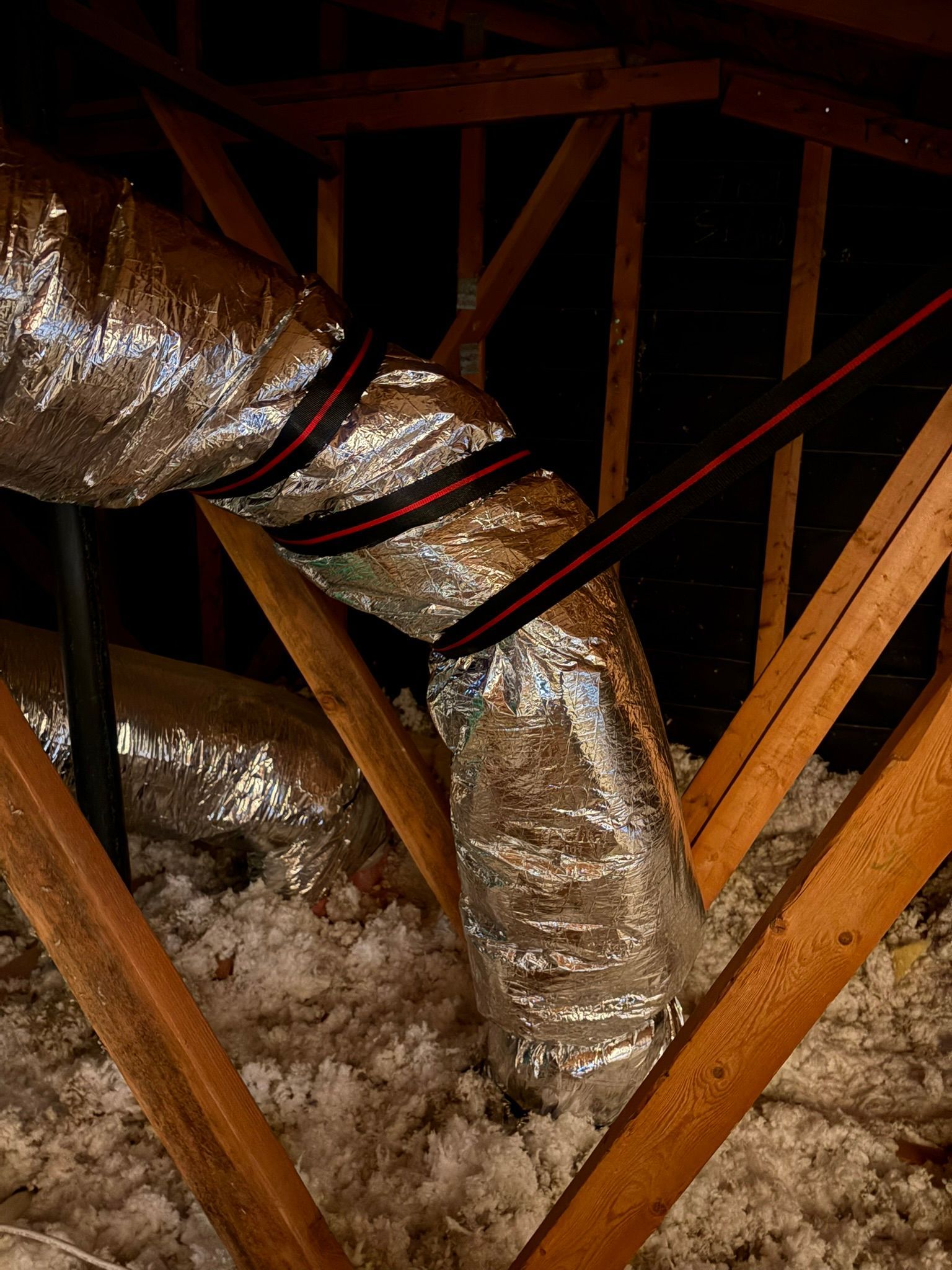 Flexible silver HVAC duct in an attic with exposed wooden rafters and insulation