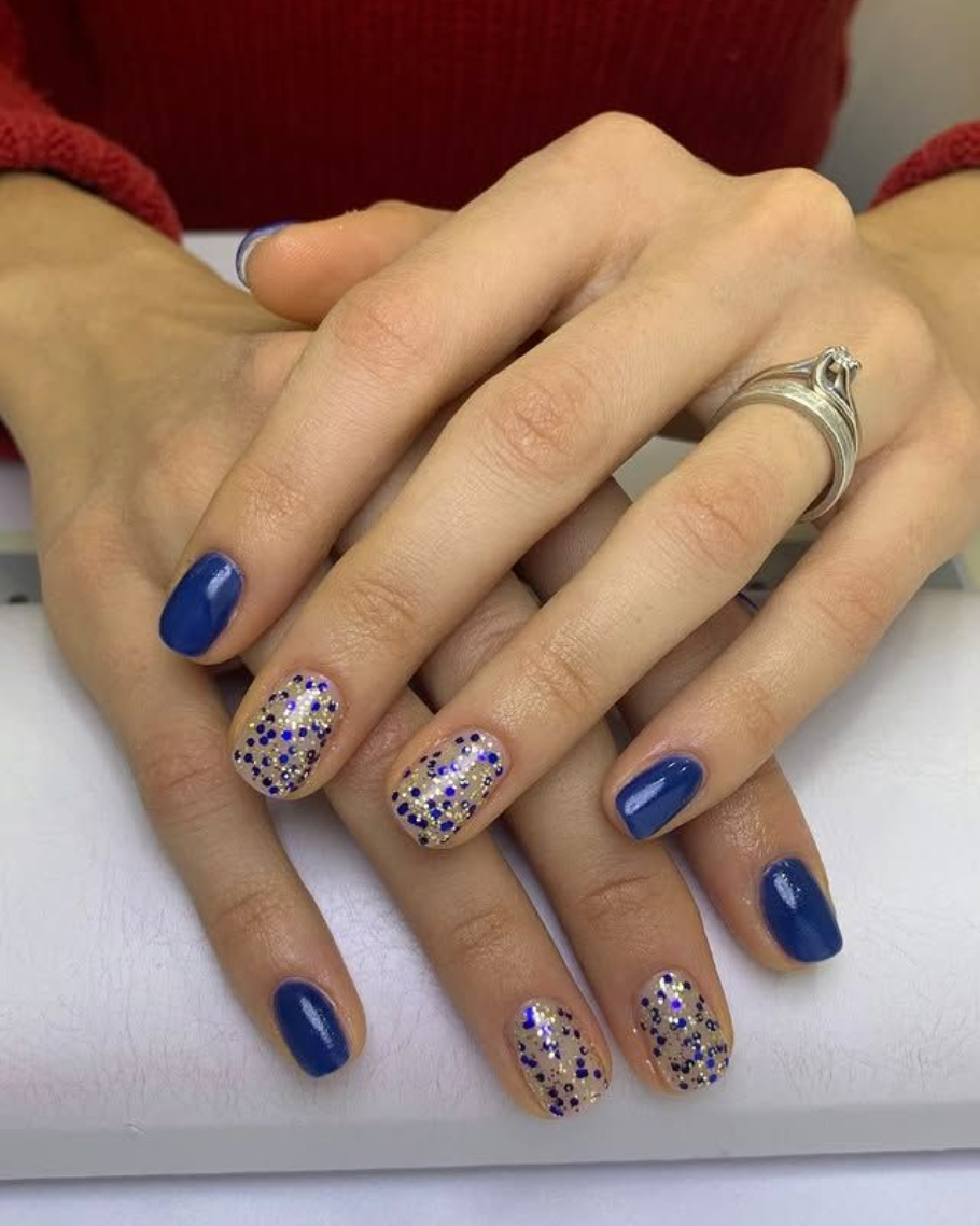 Mani con smalto blu, due unghie con glitter trasparenti sopra, anello d'argento.