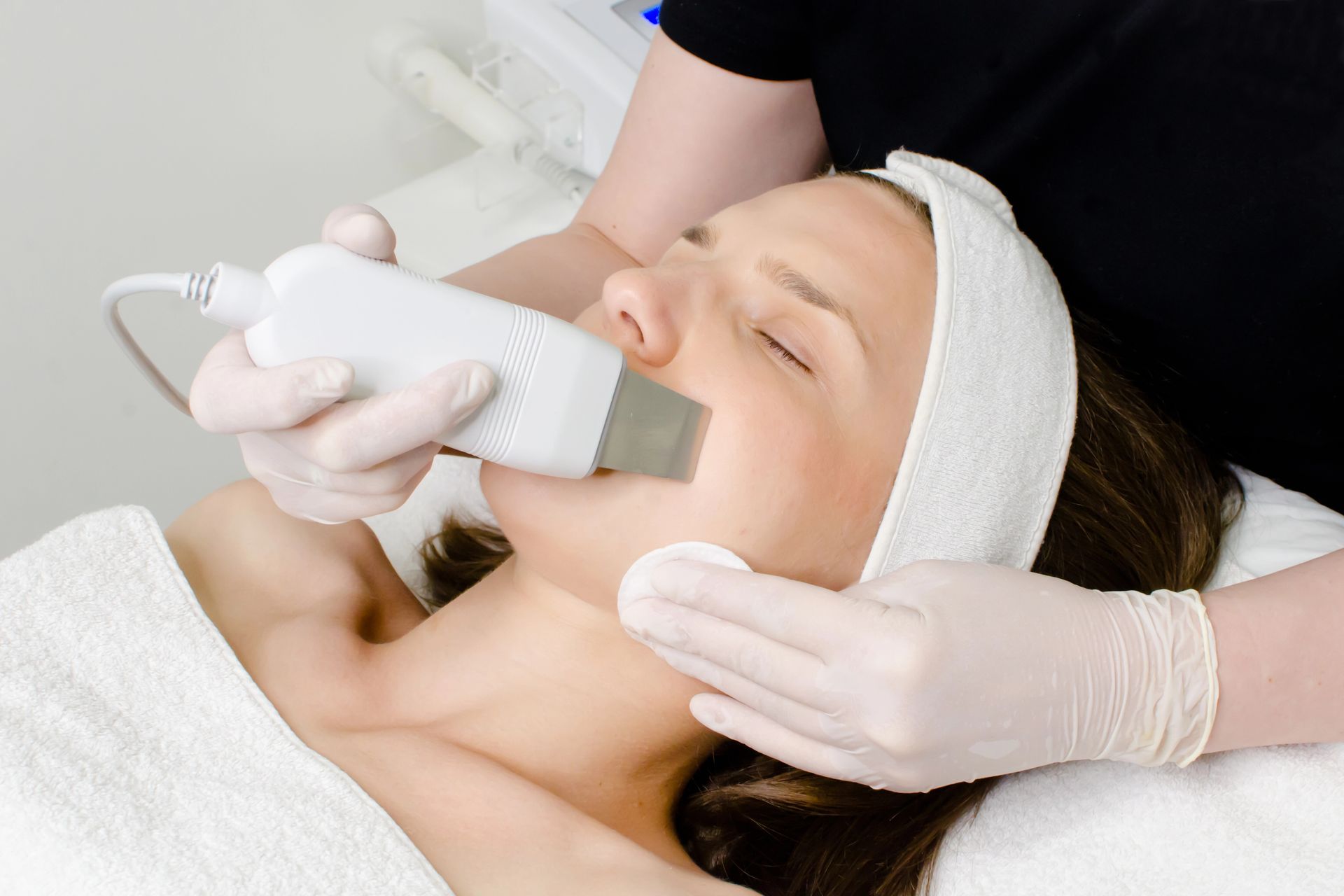 Donna sottoposta a un trattamento viso; tecnico che utilizza un dispositivo per esfoliare la pelle in un centro benessere.