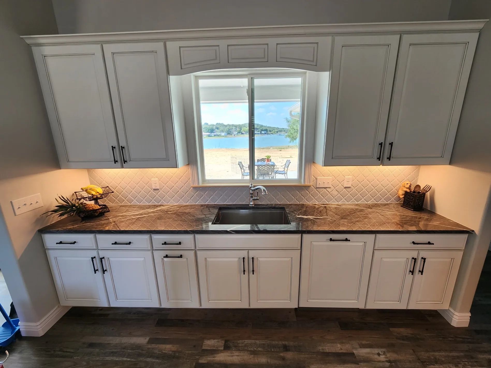 White kitchen wall with built-in cabinets, dark countertops, and a window above the sink.