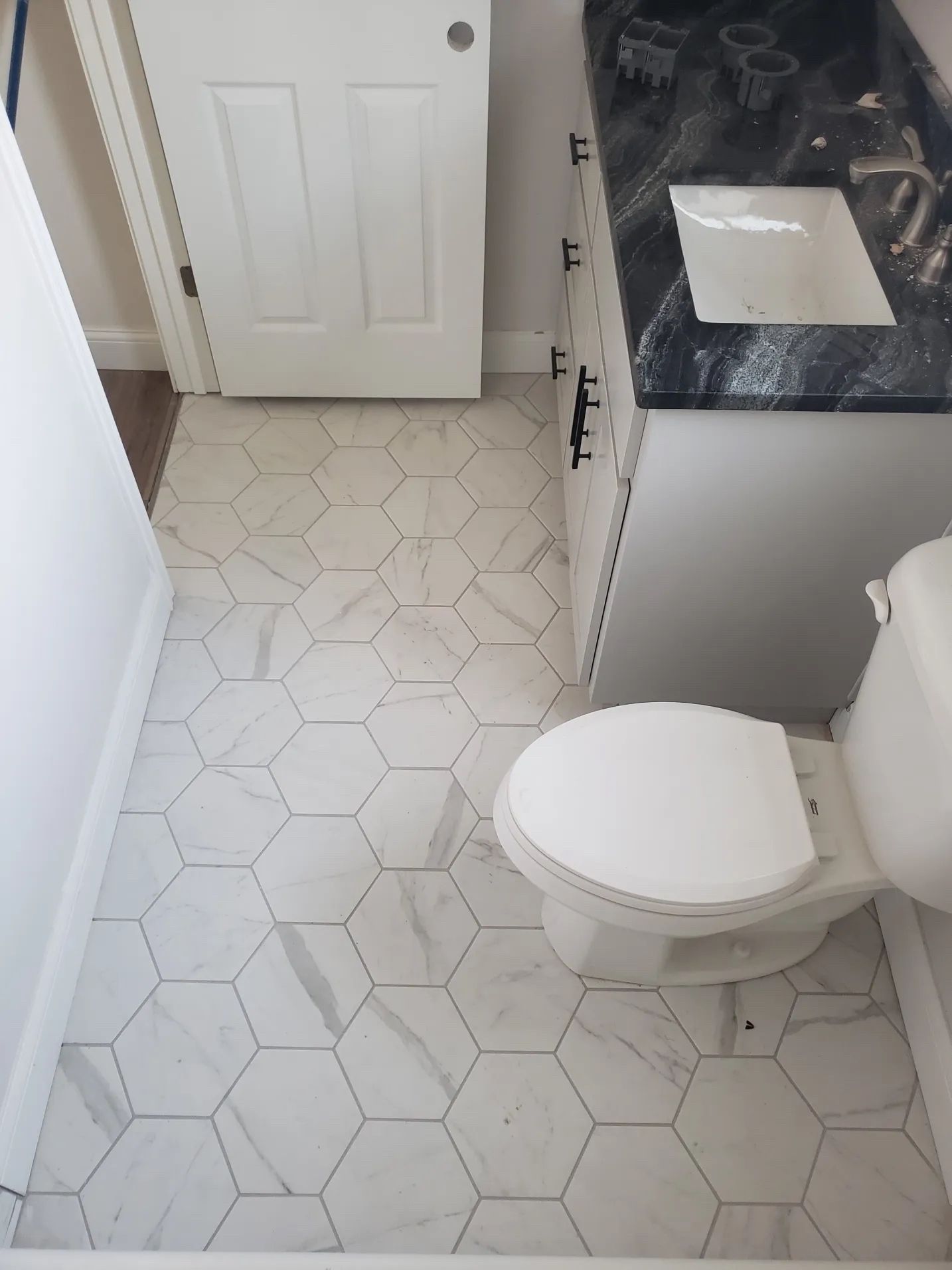 Small bathroom with white toilet, hexagon tile floor, vanity sink, and partially open door.