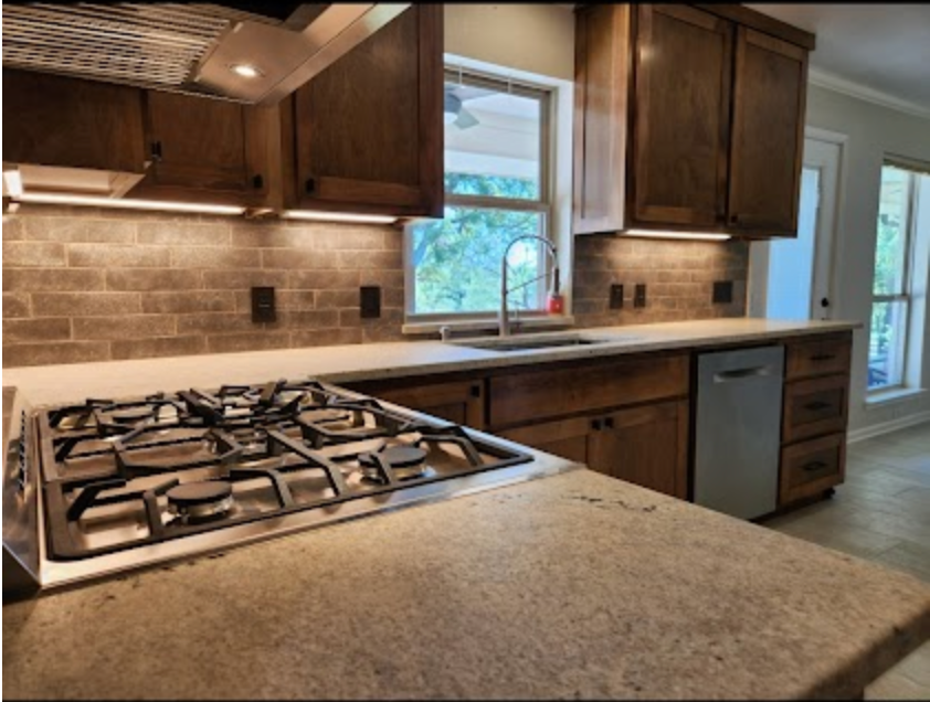 Modern kitchen with granite island, gas cooktop, wood cabinets, tile backsplash, and a window over the sink.