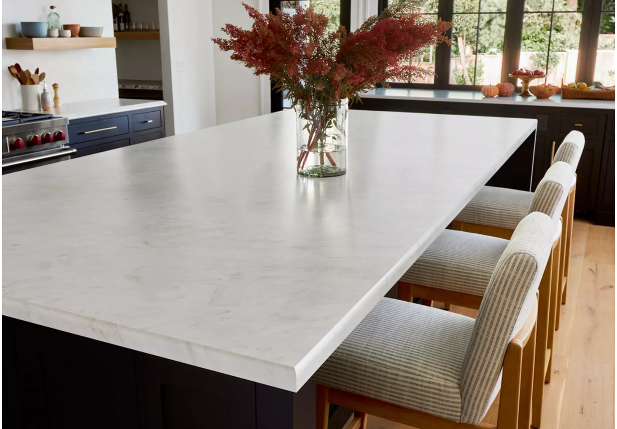 Modern kitchen with large white island, striped stools, and a vase of red flowers on top
