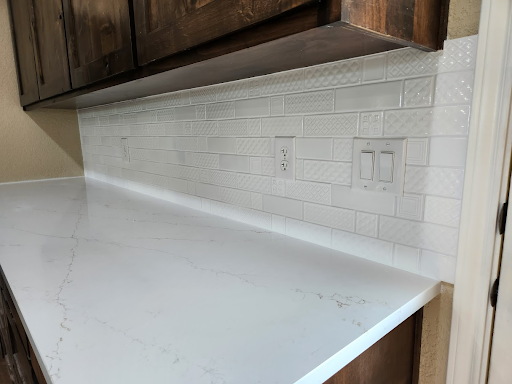 White kitchen countertop with subway tile backsplash, wood cabinets, and outlets beneath upper cabinets