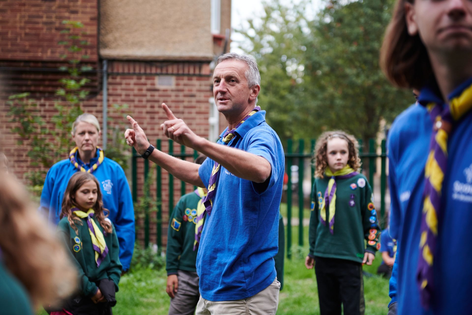 A man in a blue shirt is standing in front of a group of boy scouts.