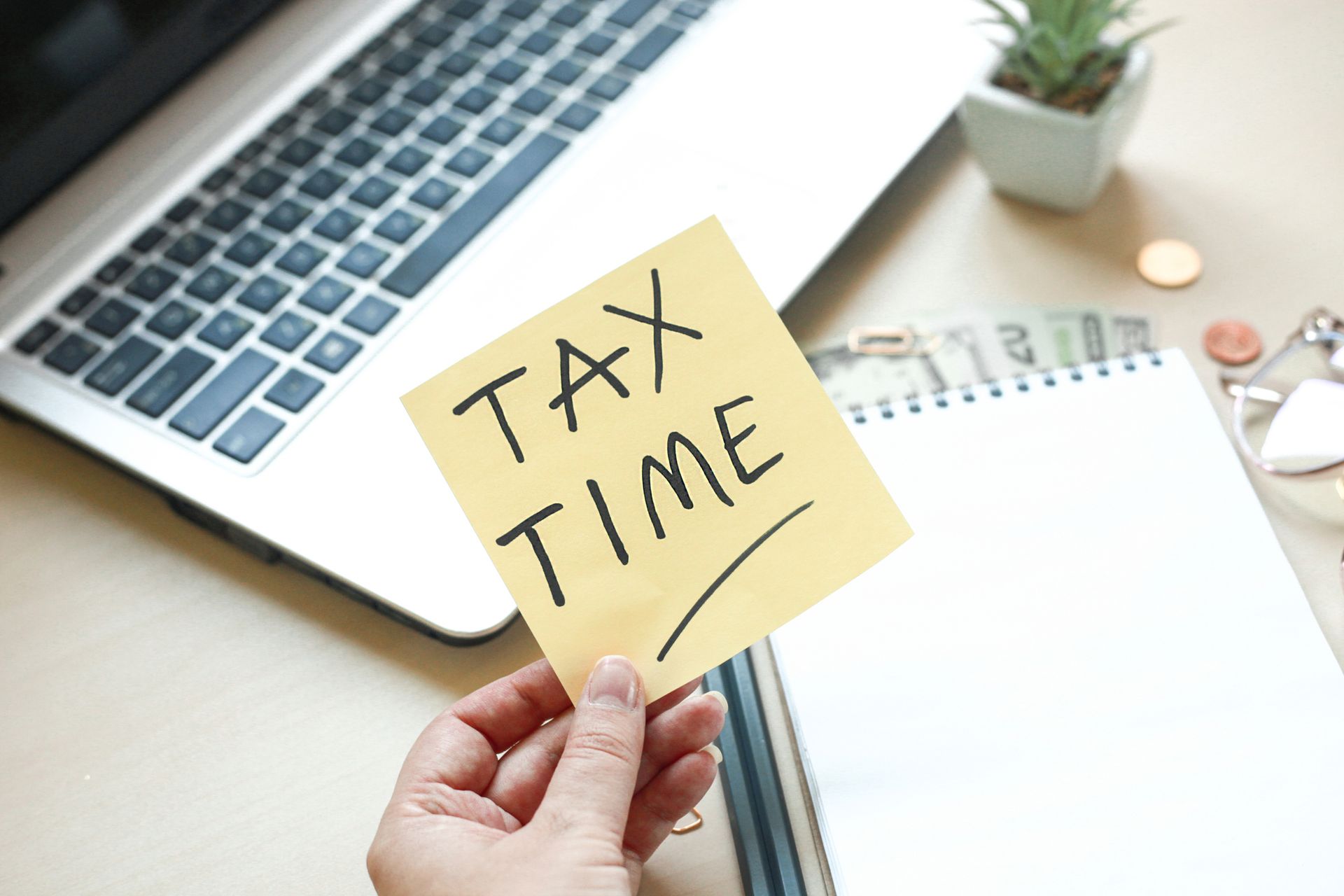 A person is holding a sticky note that says tax time in front of a laptop.