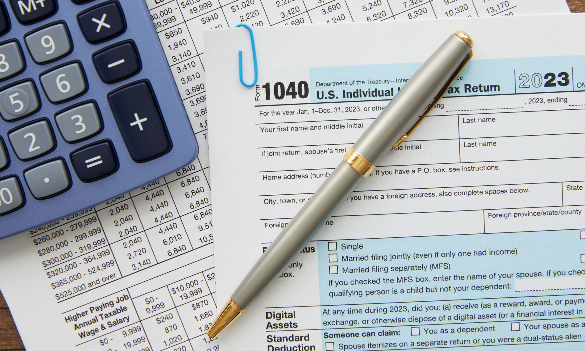 A pen sits on top of a 1040 tax form next to a calculator