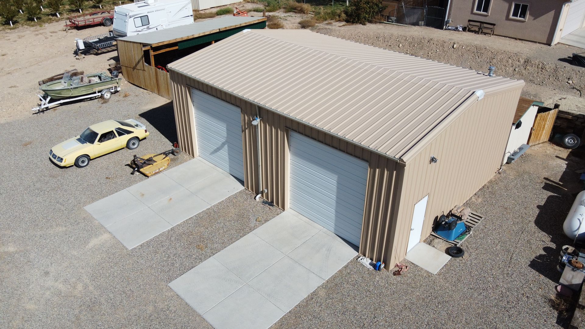 A black metal building with a white garage door is sitting in the middle of a muddy field.