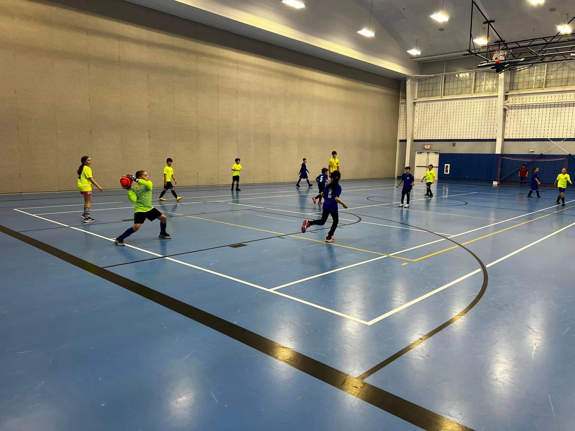 Indoor futsal game on a blue court with players in yellow and navy uniforms near the goal
