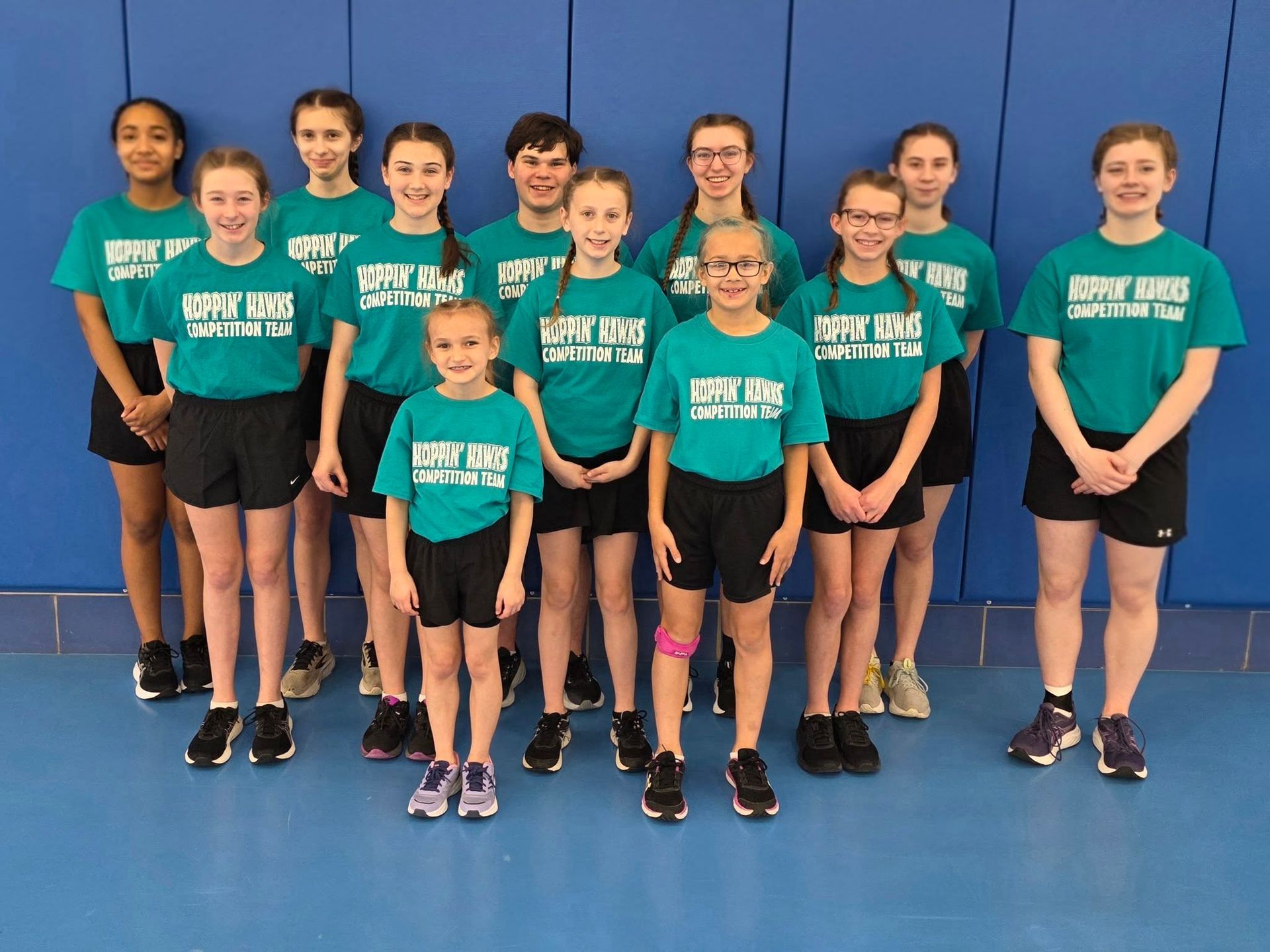 Group of youth athletes posing in teal team shirts and black shorts in a gymnasium